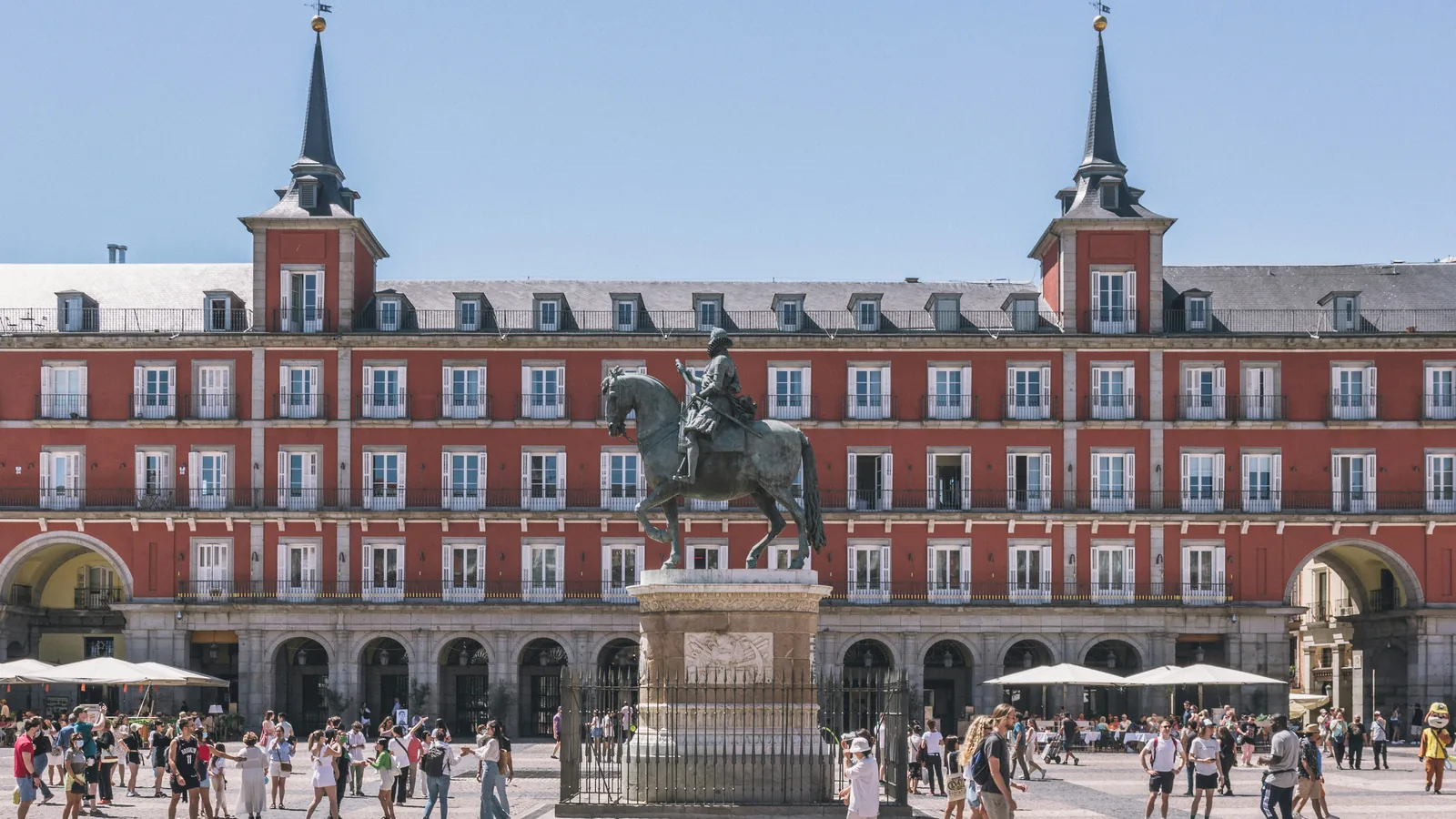 Historic arcaded square in central Madrid with a bronze equestrian statue and people crossing the pavement