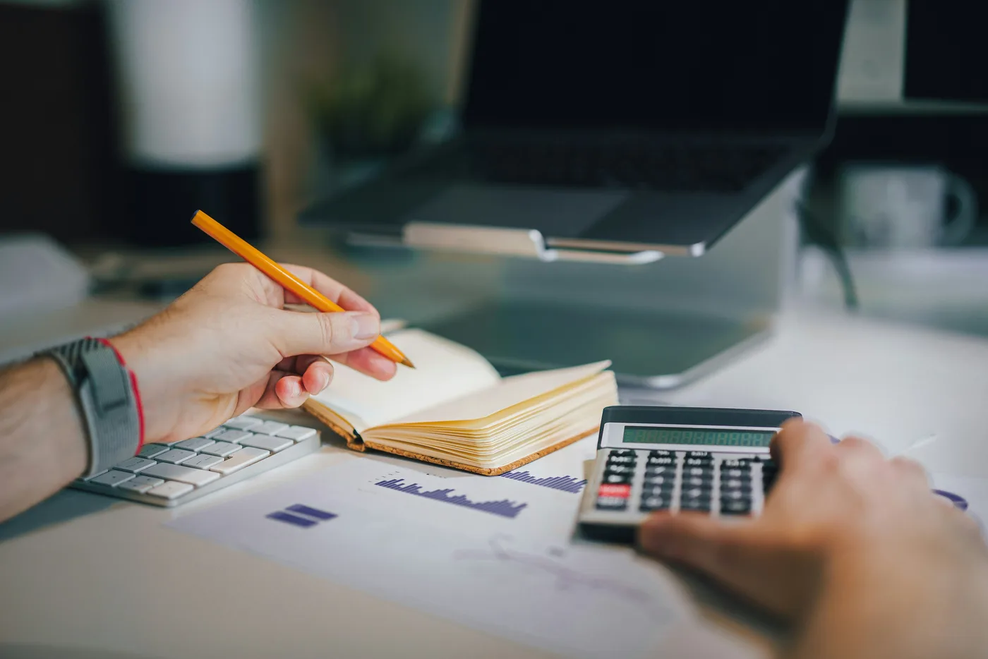 Persona tomando notas junto a una calculadora y gráficos impresos